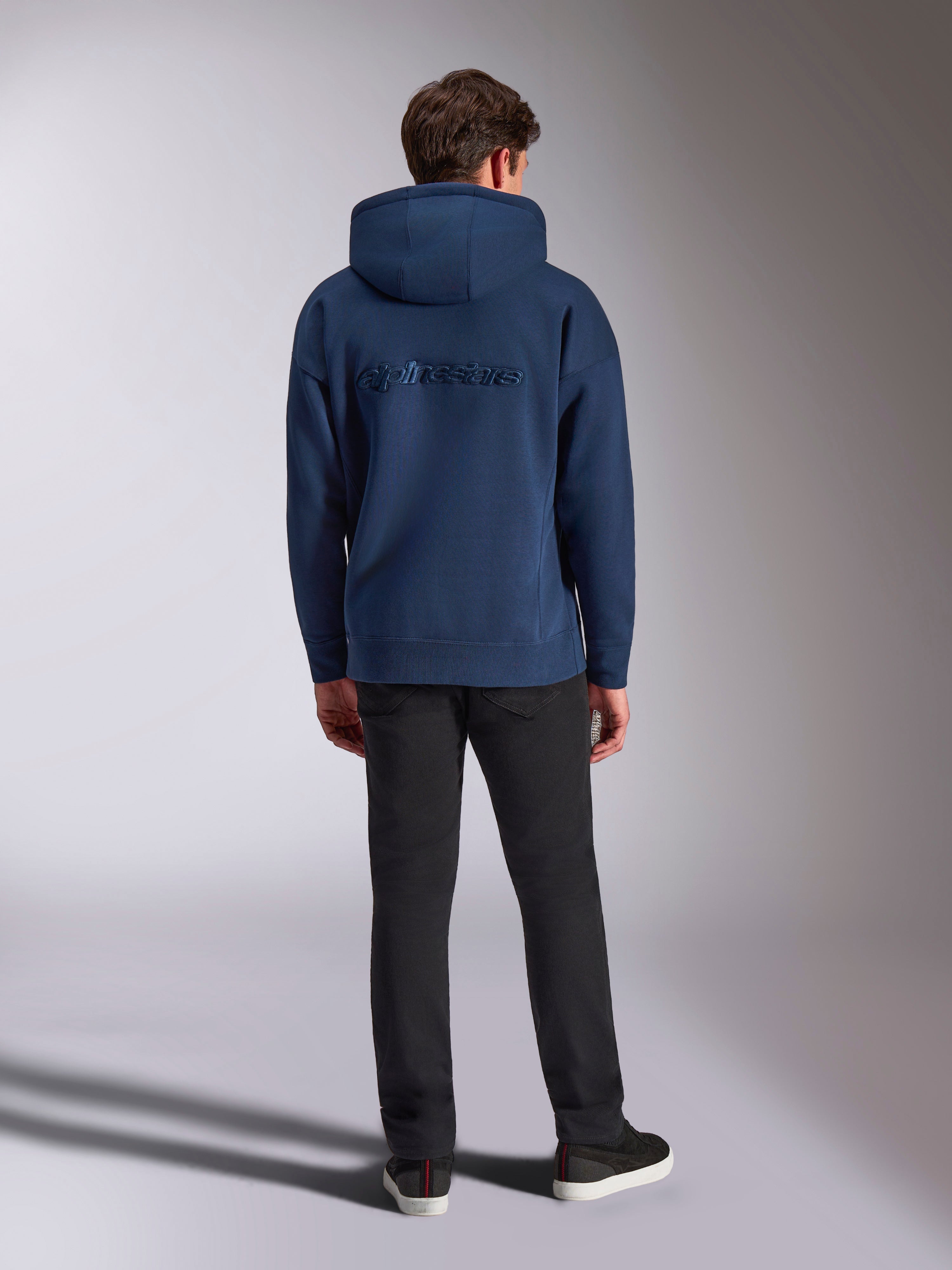 Alpinestars Emergent Oversized Hoodie, lässige Streetwear, Marineblau, farblich abgestimmter Alpinestars-Schriftzug auf dem Rücken gestickt, Oversized-Passform mit Kapuze, kombiniert mit schwarzer Hose, Rückansicht