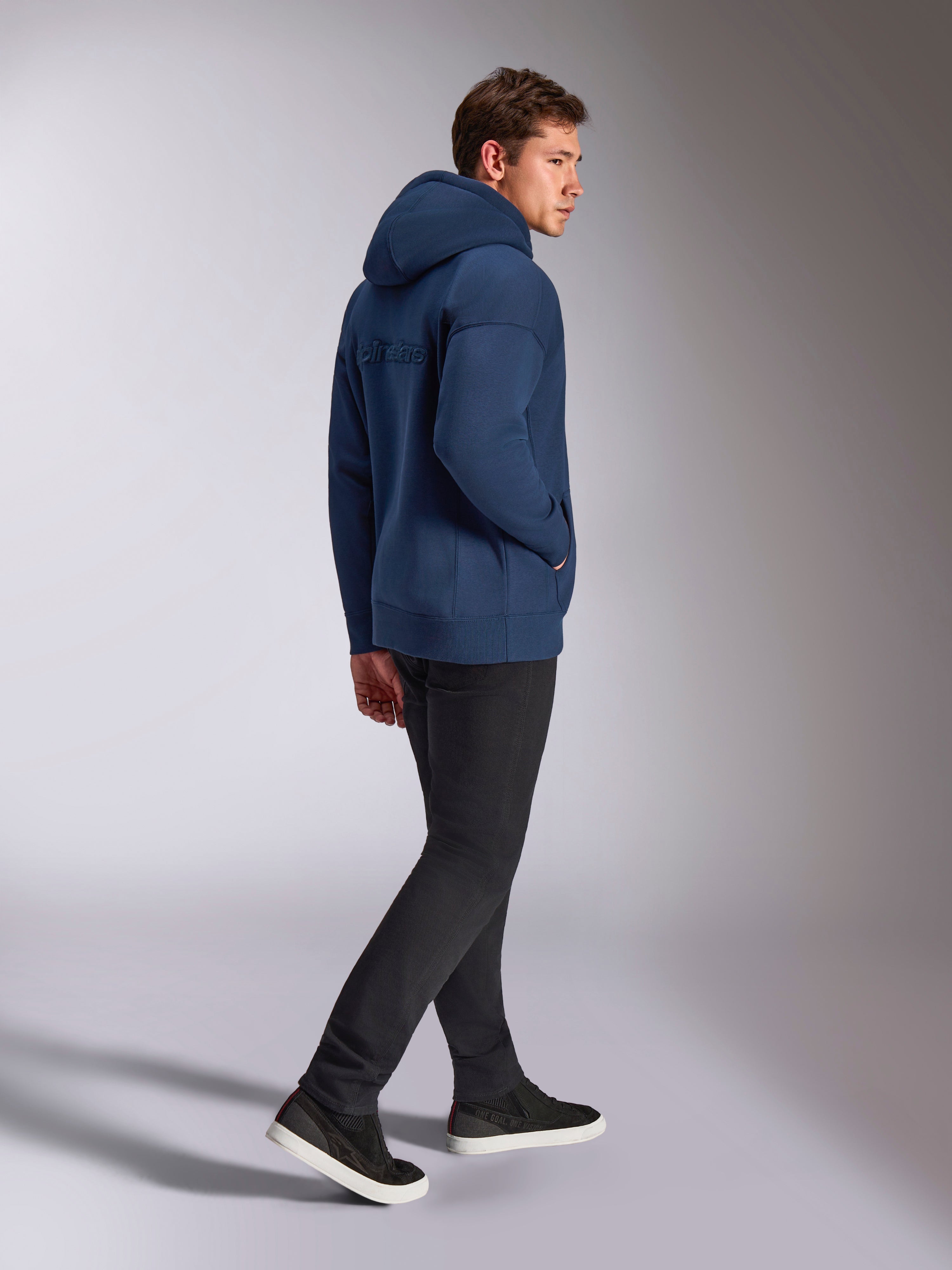 Alpinestars Emergent Oversized Hoodie in Marineblau, Rückansicht mit 3D-gesticktem Alpinestars-Wortlogo, Oversized-Fleece-Passform mit Kapuze mit Kordelzug, getragen mit schwarzer Hose, lässige vom Motorsport inspirierte Streetwear
