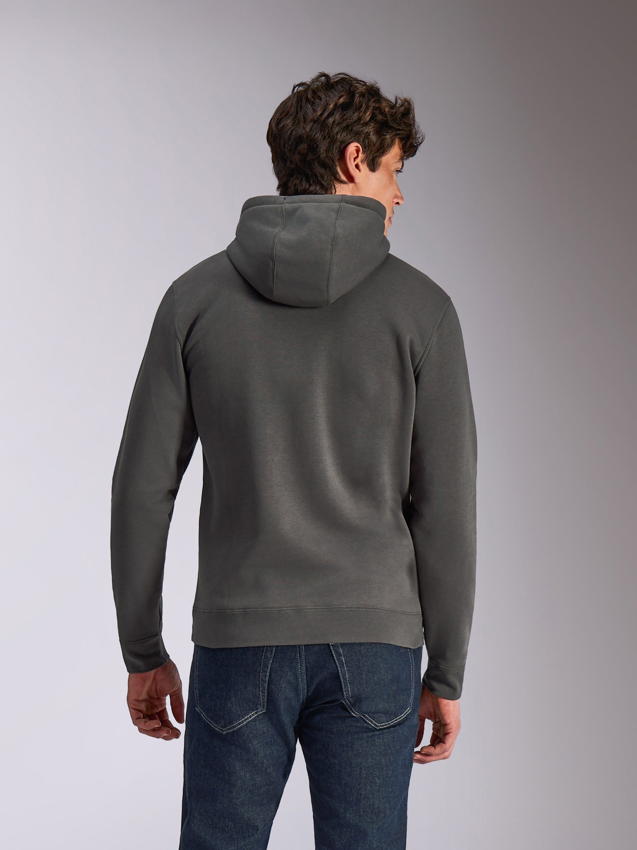 Alpinestars Ellipsoid Hoodie, Gunmetal-Grau, lässige Sportbekleidung, Rückansicht eines Mannes, der einen Fleece-Kapuzenpullover trägt, Rippbündchen an Saum und Ärmelabschlüssen, kombiniert mit blauen Jeans