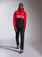 Alpinestars Parallel Hoodie, Fleece-Kapuzenpullover mit Color-Blocking, Rot und Schwarz, mit weißem Alpinestars-Wortlogo auf der Brust und Astars-Logo auf der linken Brust, getragen von einem Model mit schwarzer Hose und High-Top-Sneakern, lässige Motorsport-Streetwear