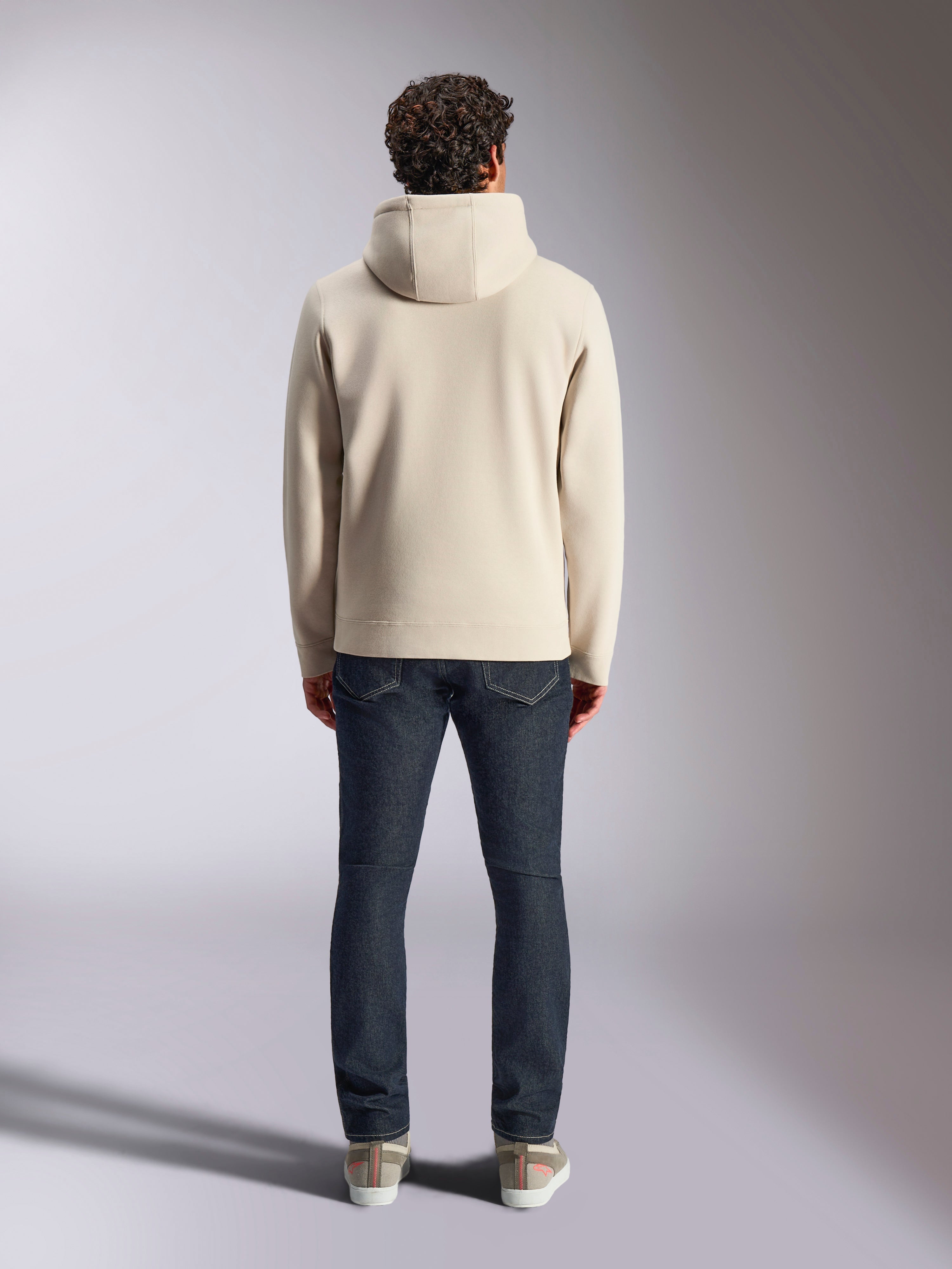 Alpinestars Pulse Kapuzenpullover, lässige Streetwear, Off White, Rückansicht an einem Model in dunklen Denim-Jeans und Sneakern, Fleece-Kapuzenpullover mit Rippbündchen und Saum