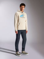 Alpinestars Pulse Hoodie, Off White Casual-Streetwear, Kapuzenpullover aus Fleece mit blau-grauem Astars-Logo und Speed-Line-Farbverlauf, Kängurutasche, getragen von einem Model mit dunklen Denim-Jeans und High-Top-Sneakern.
