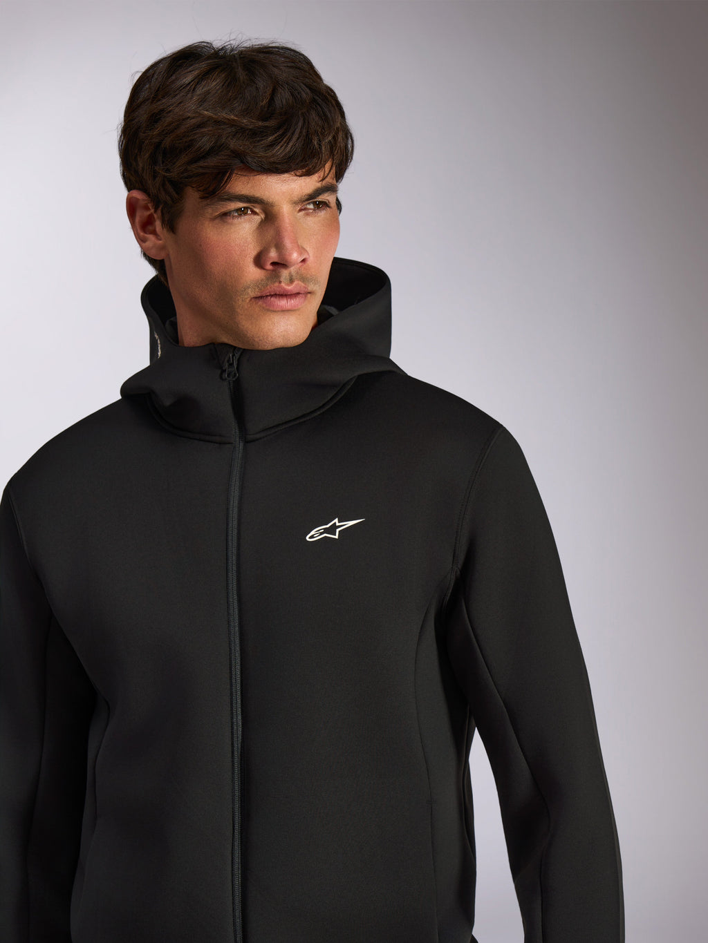 Alpinestars Cypher Hoodie, lässige Sportbekleidung, schwarzer Hoodie mit Frontreißverschluss, weißes Astars-Logo auf der Brust, Kapuzendesign mit hohem Kragen, getragen von einem männlichen Model
