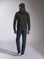 Alpinestars Cypher Hoodie, schwarzer Doppelvlies-Kapuzenpullover, Rückansicht mit kleinem weißen Alpinestars-Logo auf der unteren linken Hüfte, Kapuze mit hohem Kragen, kombiniert mit dunkelblauer Jeans, lässige vom Motorsport inspirierte Streetwear