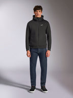 Modell trägt den Alpinestars Cypher Hoodie, schwarzer Fleece-Hoodie mit Front-Reißverschluss, hochgeschlossene Kapuze mit kleinem weißen Astars-Logo auf der Brust, kombiniert mit dunkler Denim-Jeans und schwarzen Sneakern, lässige Motorsport-inspirierte Streetwear
