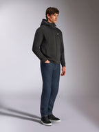 Alpinestars Cypher Hoodie, lässige Streetwear, schwarzer Kapuzenpullover mit Reißverschluss, männliches Model in dunkelblauen Jeans und schwarzen Sneakern, hochgeschlossene Kapuze mit Alpinestars-Wortlogo, kleines weißes Astars-Logo auf der Brust, eleganter vom Motorsport inspirierter Lifestyle-Look