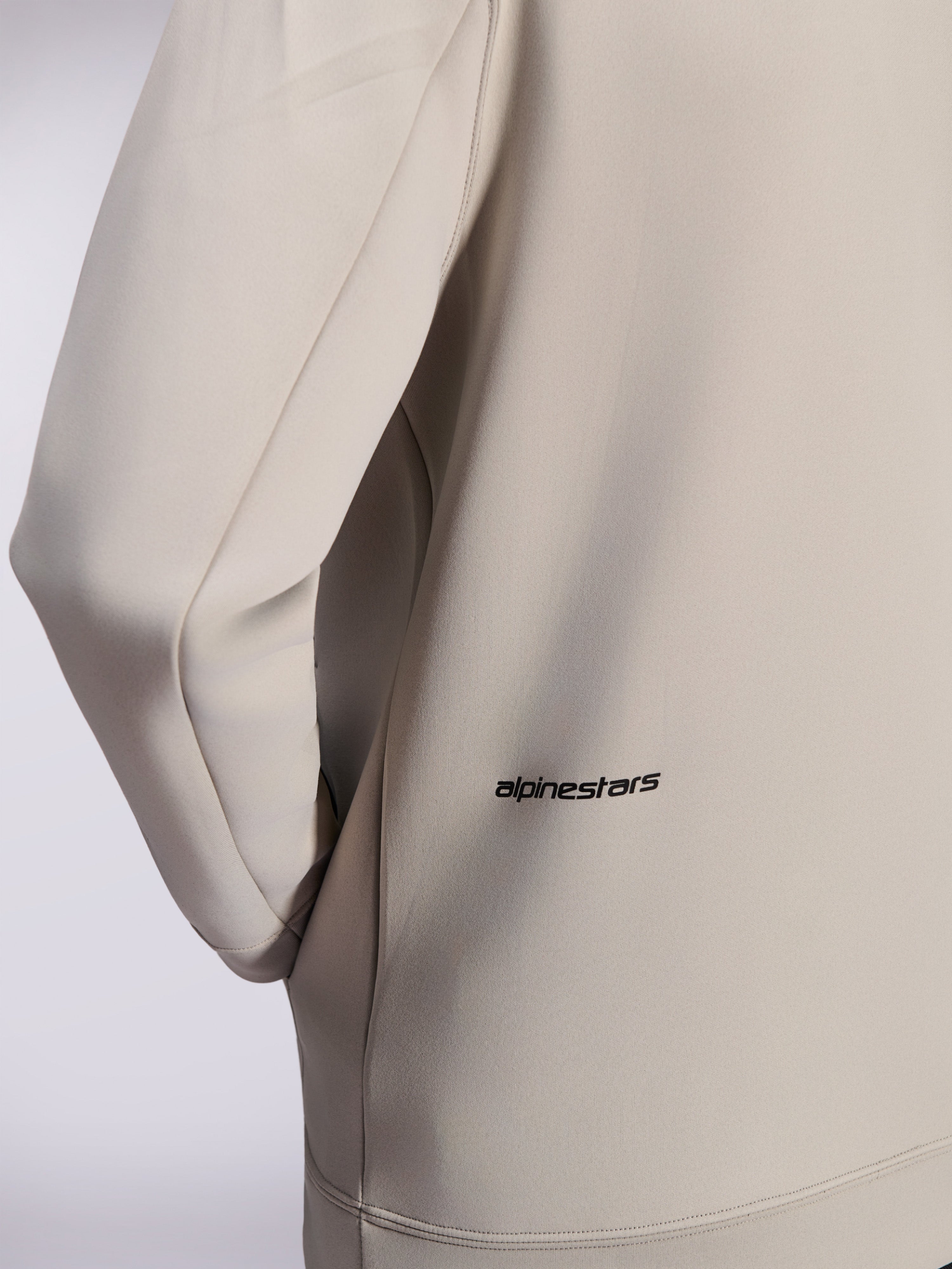 Alpinestars Cypher Hoodie, Zip-Hoodie aus Double-Face-Fleece, Cement Gray, Nahaufnahme des kleinen schwarzen Alpinestars-Wortlogos am unteren Rücken, Detail einer Nahttasche und glatte Stofftextur
