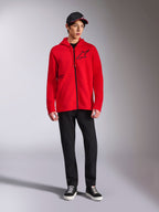 Alpinestars Transverse Hoodie, Red full-zip fleece hoodie, black Astars logo on chest and One Goal print on side, worn by male model with black pants and cap, casual motorsport-inspired streetwear