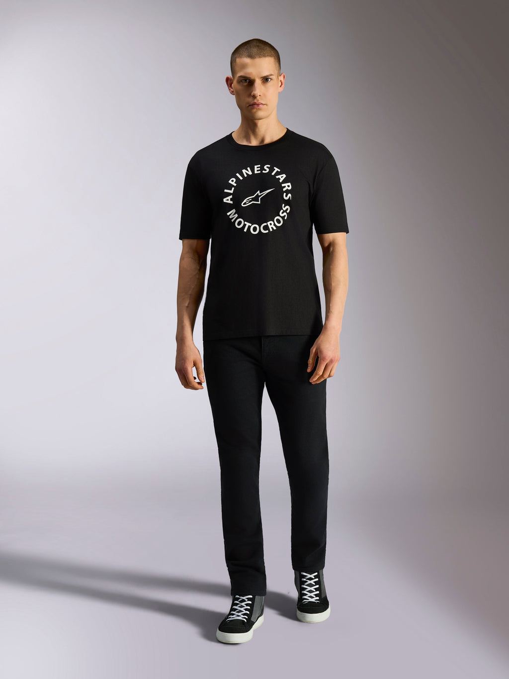Alpinestars MX CSF Tee, Kurzarm-T-Shirt, Schwarz, weiße kreisförmige Alpinestars Motocross-Grafik, getragen von einem Model mit schwarzer Hose und Sneakern, lässige Motorsport-Streetwear