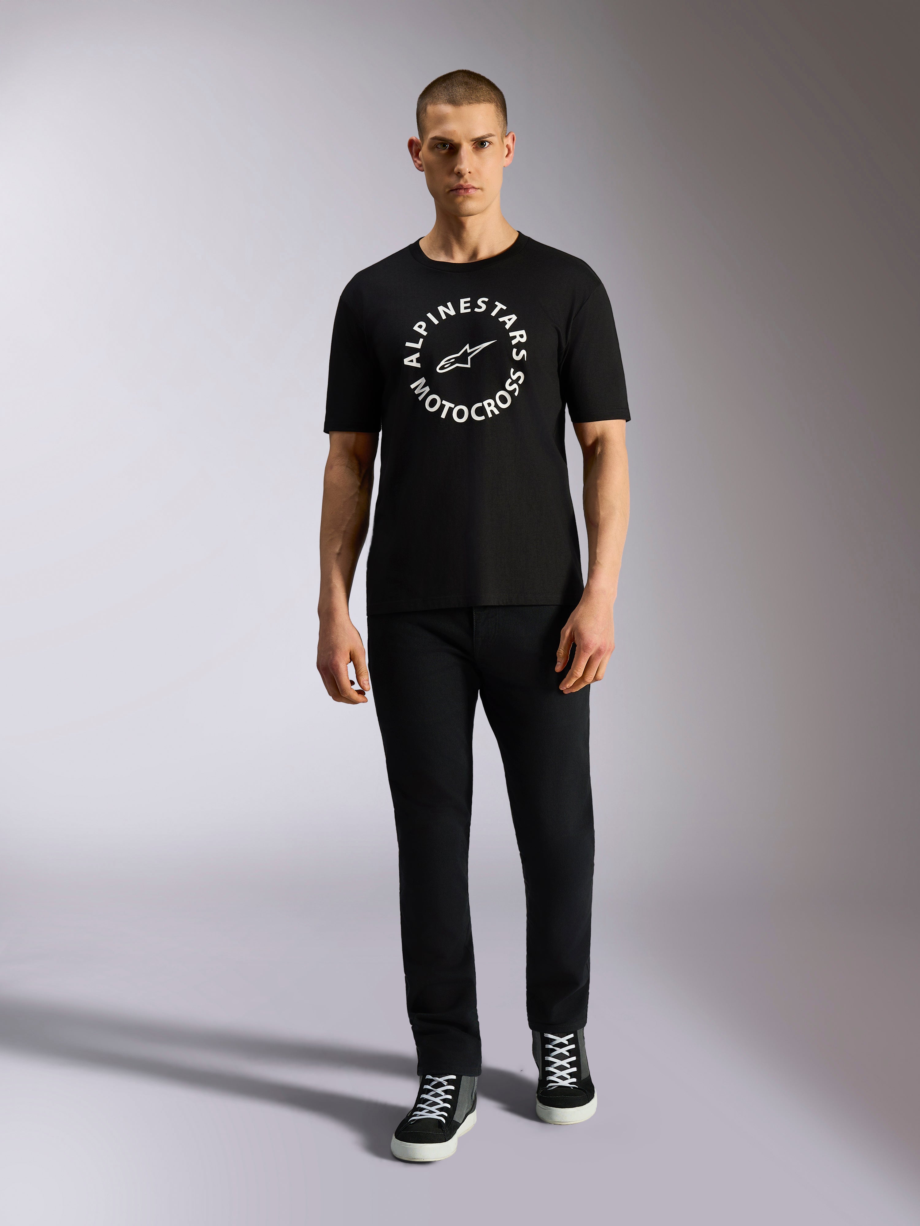 Alpinestars MX CSF Tee, Kurzarm-T-Shirt, Schwarz, weiße kreisförmige Alpinestars Motocross-Grafik, getragen von einem Model mit schwarzer Hose und Sneakern, lässige Motorsport-Streetwear