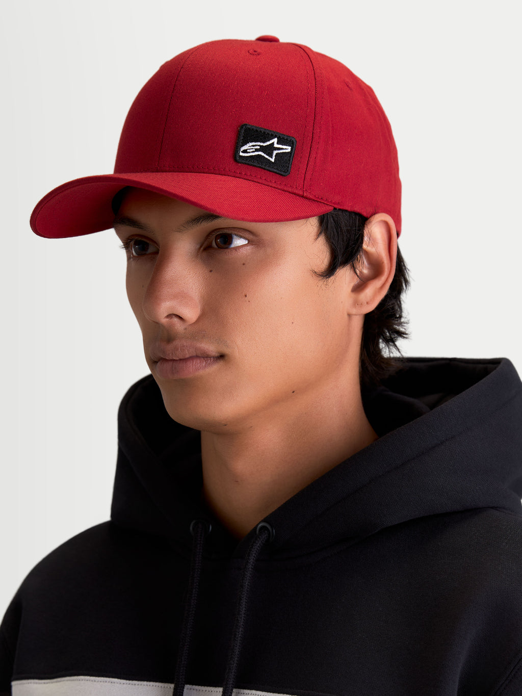 Alpinestars Pivot Kappe, Lifestyle-Sportswear-Kappe für Herren und Damen, Dunkelrot, mit gebogenem Schirm, strukturierter Krone und einem kleinen schwarzen Astars Logo-Stickpatch auf der Vorderseite, am Model getragen.