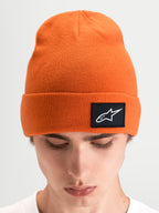 Alpinestars Augment Cuff Mütze, orangefarbene Sportswear-Strickmütze mit tiefer Passform und schwarzem Astars-Logo-Patch am Umschlag, getragen von einem männlichen Model