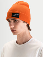 Alpinestars Augment Cuff Mütze, orange Strickmütze mit schwarz-weißem Astars-Logo-Patch, getragen von einem Model in legerer Freizeitbekleidung