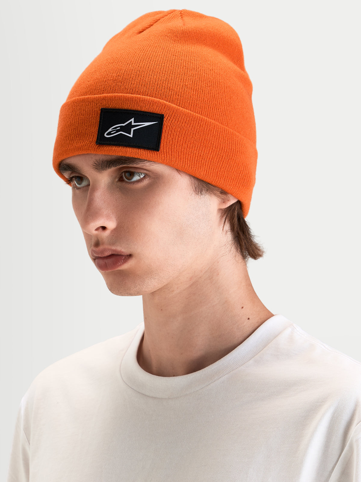 Alpinestars Augment Cuff Mütze, orange Strickmütze mit schwarz-weißem Astars-Logo-Patch, getragen von einem Model in legerer Freizeitbekleidung