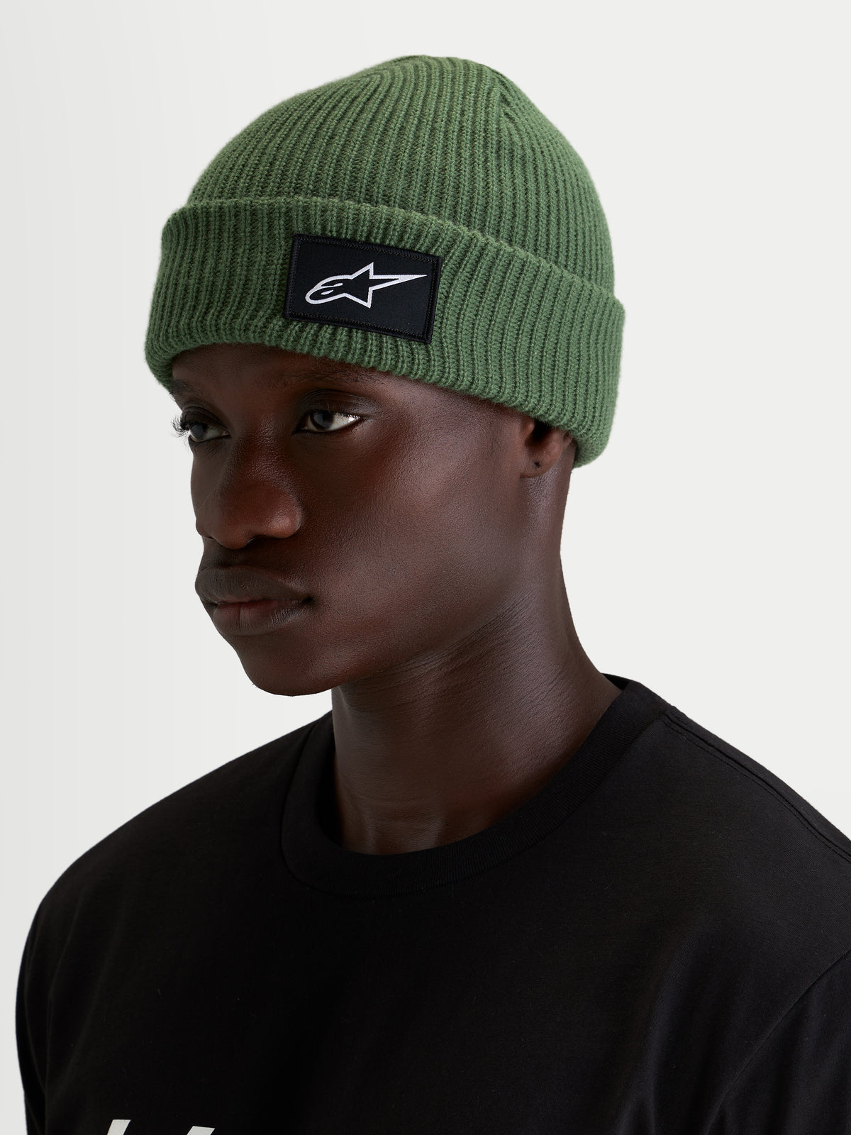 Alpinestars Unload Rib Cuff Mütze, grüne Casual-Wintermütze, getragen von einem Model, mit Rippstrick-Konstruktion und schwarz-weißem SAstars-Vorderaufnäher