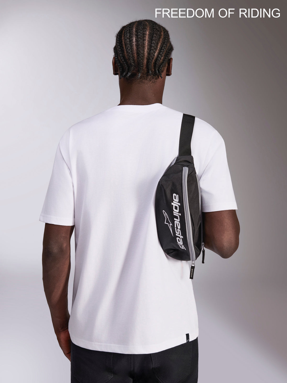Alpinestars Only Linear Hüfttasche, Urban Sportswear Tasche, Schwarz und Weiß, 2L Fassungsvermögen, 100% Polyester mit Alpinestars-Logo, getragen als Crossbody-Schultertasche auf einem Modell für Alltag und Reisen.