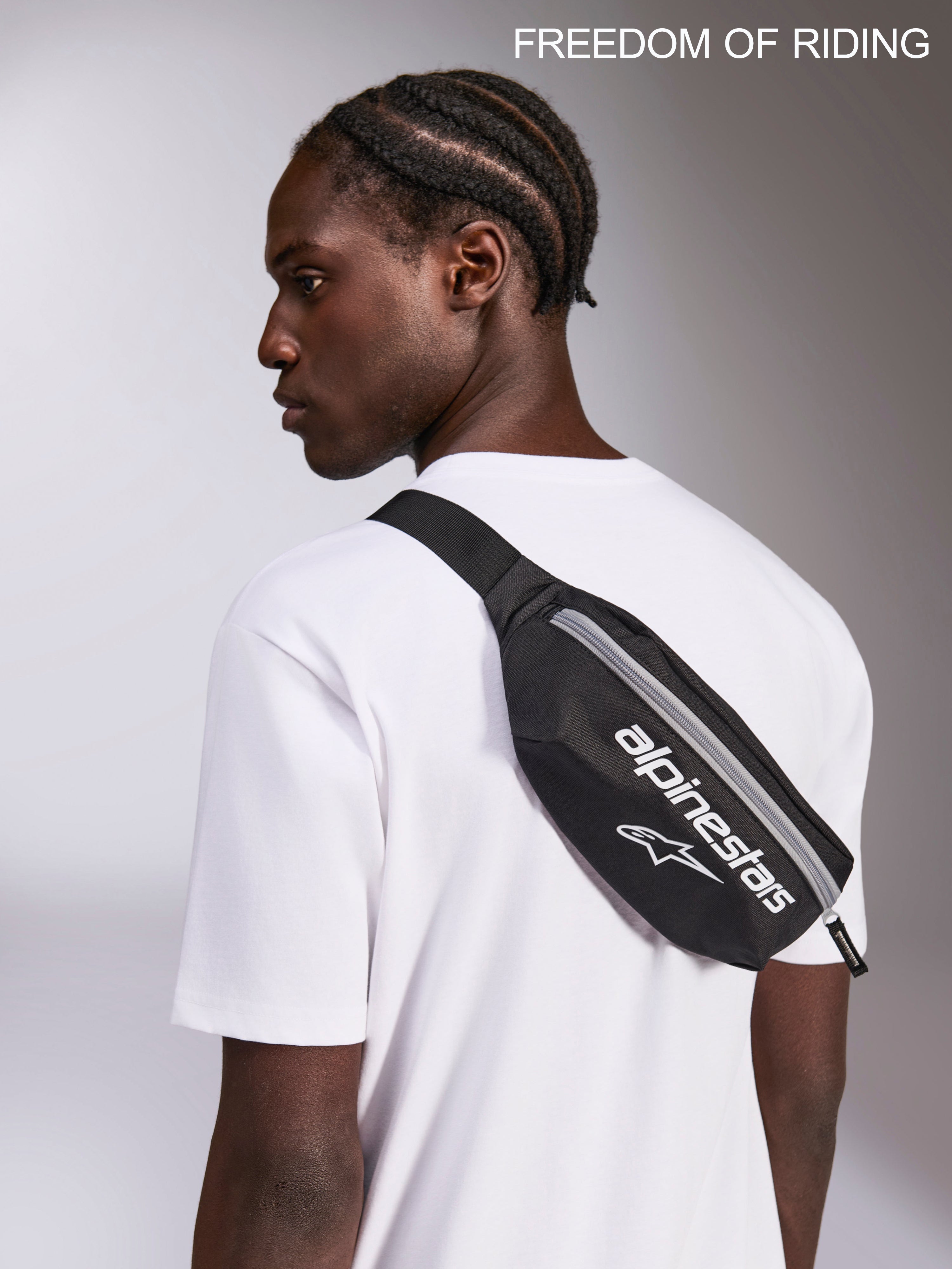 Alpinestars Only Linear Hüfttasche, Sportswear Crossbody-Hüfttasche, Schwarz und Weiß, 2L Kapazität, robustes 600D Polyester, von einem Modell über einem weißen T-Shirt getragen für urbanen Pendelverkehr und den Alltag.