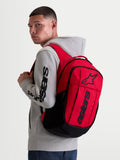 Alpinestars GFX Boss Rucksack, 20L Urban Sportswear Tagesrucksack, Rot und Schwarz, am Modell in grauem Kapuzenpullover gezeigt. Mit strapazierfähiger 600D Polyester-Konstruktion, erhabenem Silikon-Astars-Grafik-Branding und internem Laptopfach. Ideal für das tägliche Pendeln und den Alltag.