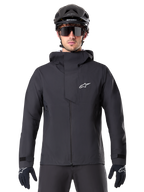 Alpinestars A-Dura Elite Wasserdichte Jacke, Schwarz, Mountainbike-Jacke, Design mit hohem Kragen und Kapuze, Frontreißverschluss mit schützender Brustklappe und weißem Logo, getragen mit schwarzem Helm und Fahrradhandschuhen, technischer Wetterschutz für Trail-Fahrten