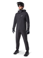 Alpinestars A-Dura Elite Wasserdichte Jacke in Schwarz, getragen von einem männlichen Fahrer mit passender schwarzer MTB-Hose, Handschuhen und Helm, technisches wasserdichtes Design, weißes Astars-Logo auf der Brust, hoher Schutzkragen