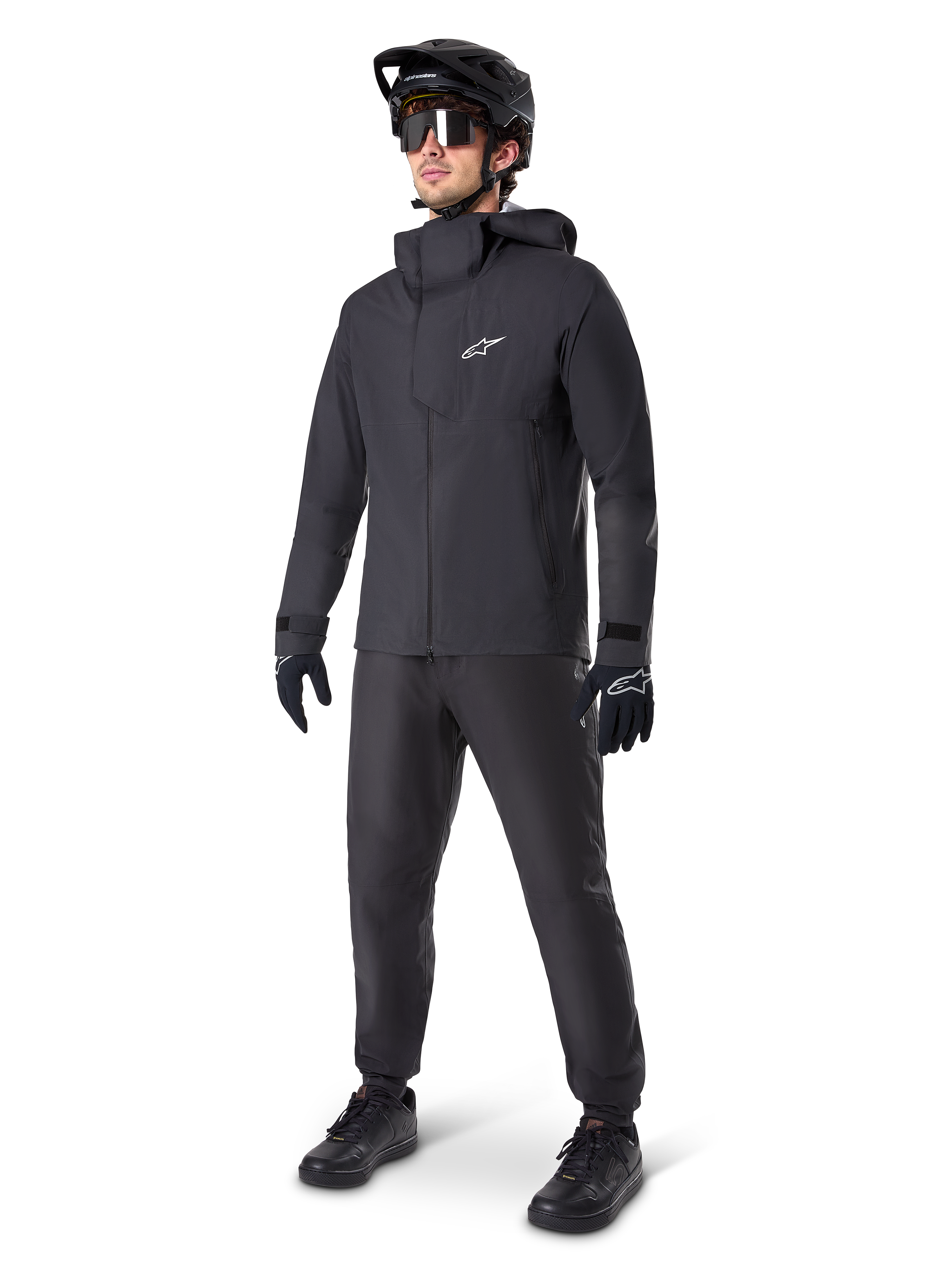 Alpinestars A-Dura Elite Wasserdichte Jacke in Schwarz, getragen von einem männlichen Fahrer mit passender schwarzer MTB-Hose, Handschuhen und Helm, technisches wasserdichtes Design, weißes Astars-Logo auf der Brust, hoher Schutzkragen