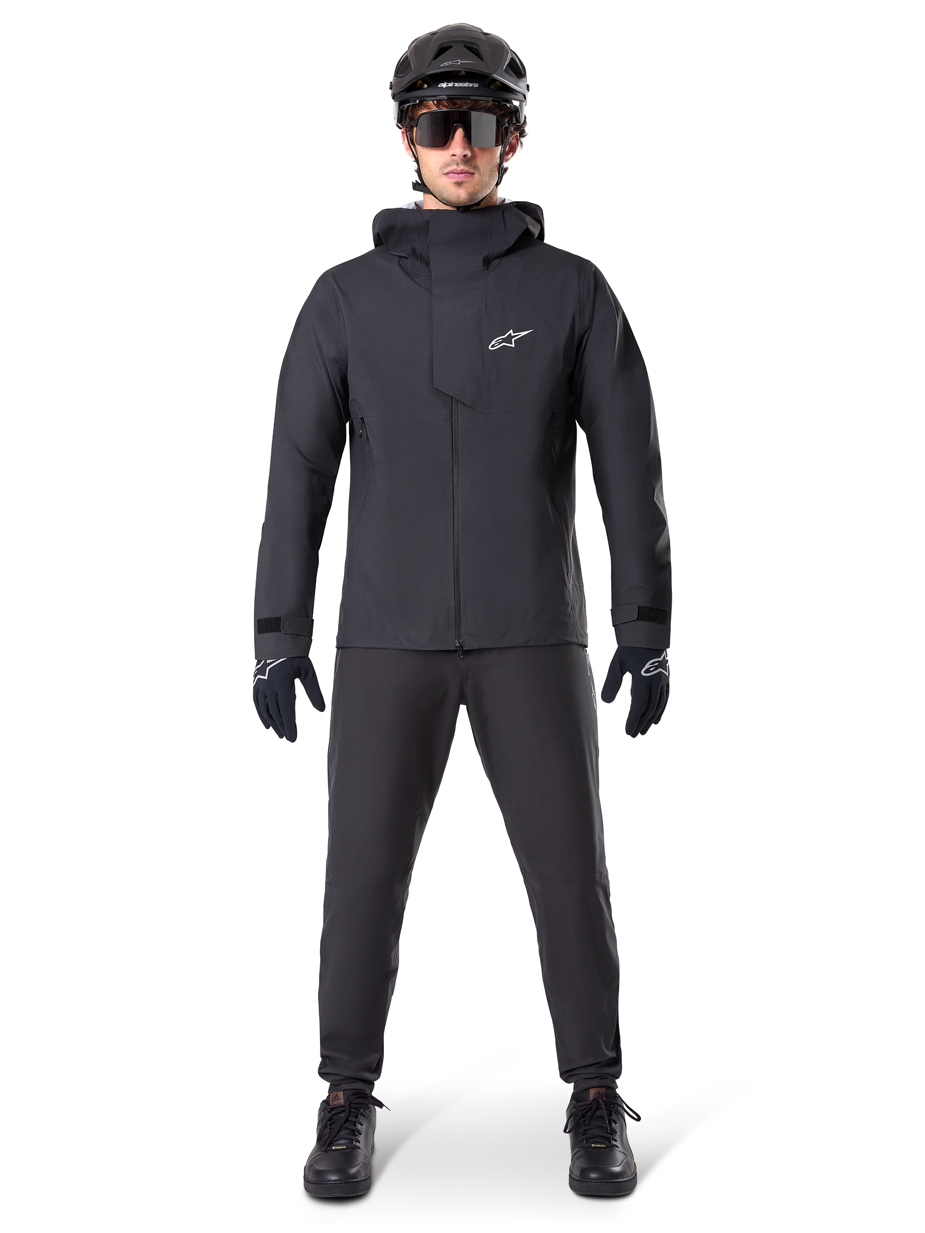 Alpinestars A-Dura Elite Wasserdichte Jacke, Schwarz, getragen mit passender Fahrradhose und Handschuhen, schwarzer Helm und Sonnenbrille, mit weißem Astars-Logo auf der Brust, leistungsstarkes technisches Design für Mountainbiking