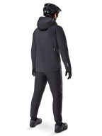 Alpinestars A-Dura Elite Wasserdichte Jacke, Schwarz, Rückansicht mit Über-dem-Helm-Kapuze und längerem, abfallendem Saum, kombiniert mit passender schwarzer MTB-Hose, Handschuhen und Helm für kompletten Allwetterschutz auf dem Trail.