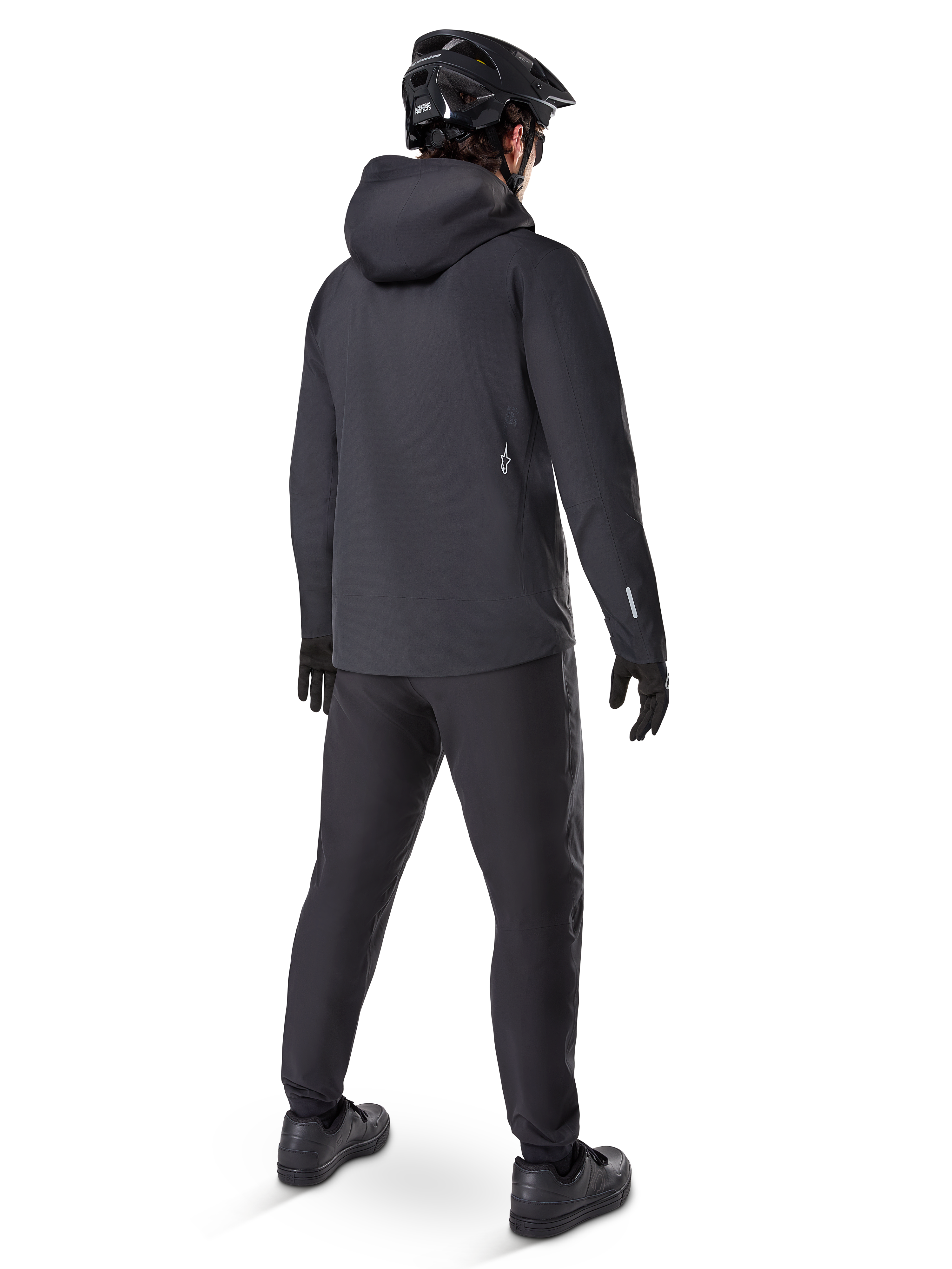 Alpinestars A-Dura Elite Wasserdichte Jacke, Schwarz, Rückansicht mit Über-dem-Helm-Kapuze und längerem, abfallendem Saum, kombiniert mit passender schwarzer MTB-Hose, Handschuhen und Helm für kompletten Allwetterschutz auf dem Trail.