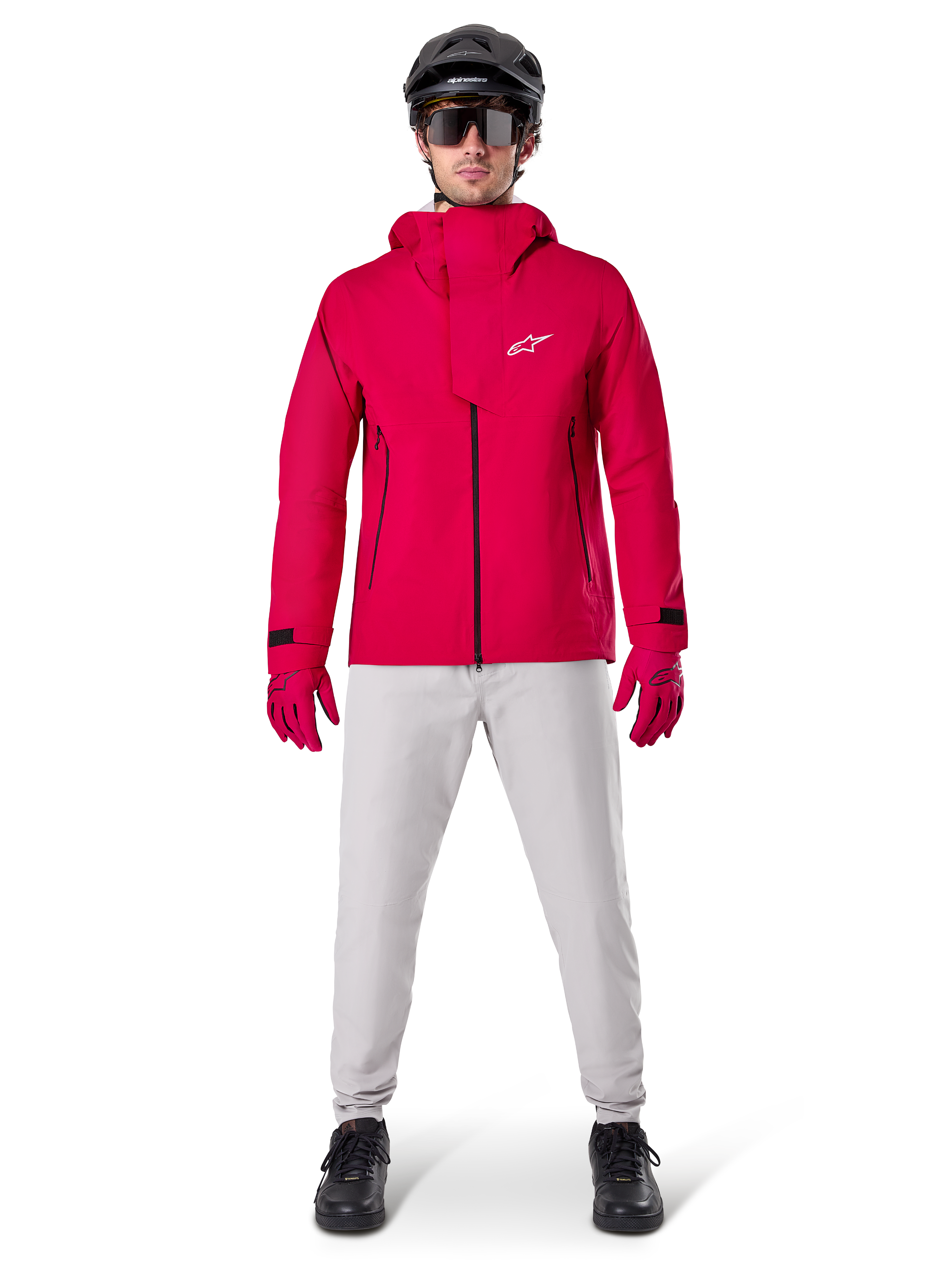 Alpinestars A-Dura Elite Waterproof Jacket, Red Fluo, technical mountain bike jacket worn with a black MTB helmet, sunglasses, matching red gloves, and light grey pants, full-body view of all-weather cycling gear