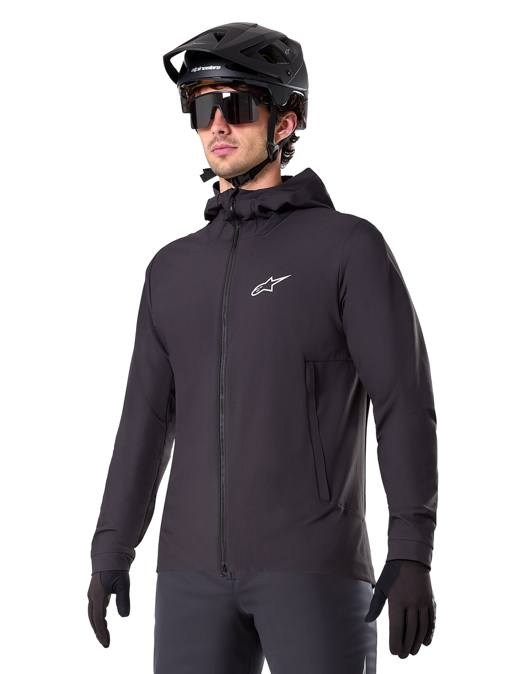 Alpinestars A-Dura Thermal Jacket, schwarze Fahrradjacke, Design mit Kapuze und Frontreißverschluss, weißes Stern-Logo auf der Brust, getragen mit schwarzem Mountainbike-Helm und Handschuhen, sportliche Funktionsbekleidung für Trailfahrten bei kaltem Wetter