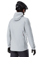 Alpinestars A-Dura Thermal Jacket, Titanium Gray, back view of a rider wearing the hooded insulated jacket, paired with a black MTB helmet and black gloves, featuring a small Alpinestars logo on the lower back, designed for cold-weather mountain biking.