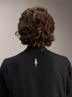 Alpinestars A-Aria Windbreaker Jacket, Black, close-up back view of upper shoulders and collar, featuring a small white logo on the center back, worn by model with wavy brown hair, minimalist performance cycling gear