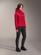 Alpinestars Stella A-Dura Elite wasserdichte Damenjacke, Red Fluo, Mountainbike-Regenjacke mit Kapuze und weißem Astars-Logo auf der Brustklappe, getragen mit schwarzer Hose und schwarzen Mountainbike-Schuhen, technische Performance-Ausrüstung für Trailfahrten