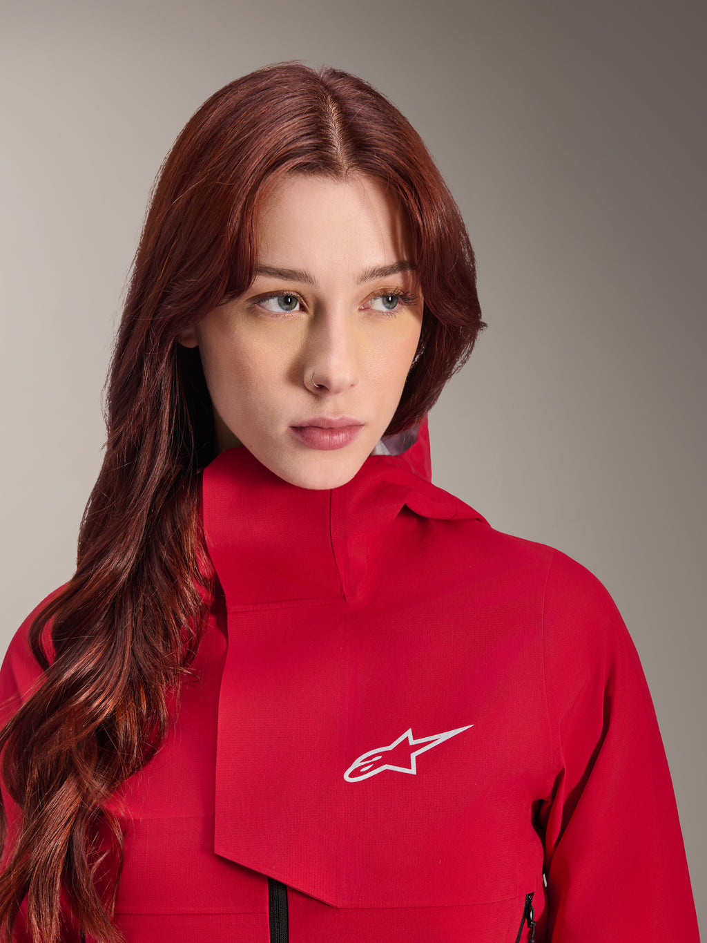 Alpinestars Stella A-Dura Elite Wasserdichte Jacke, Red Fluo, getragen von einer Frau mit langem rotem Haar, technische 3-lagige wasserdichte Jacke mit hohem Kragen und weißem Logo, Performance-Outdoor- und Mountainbike-Ausrüstung