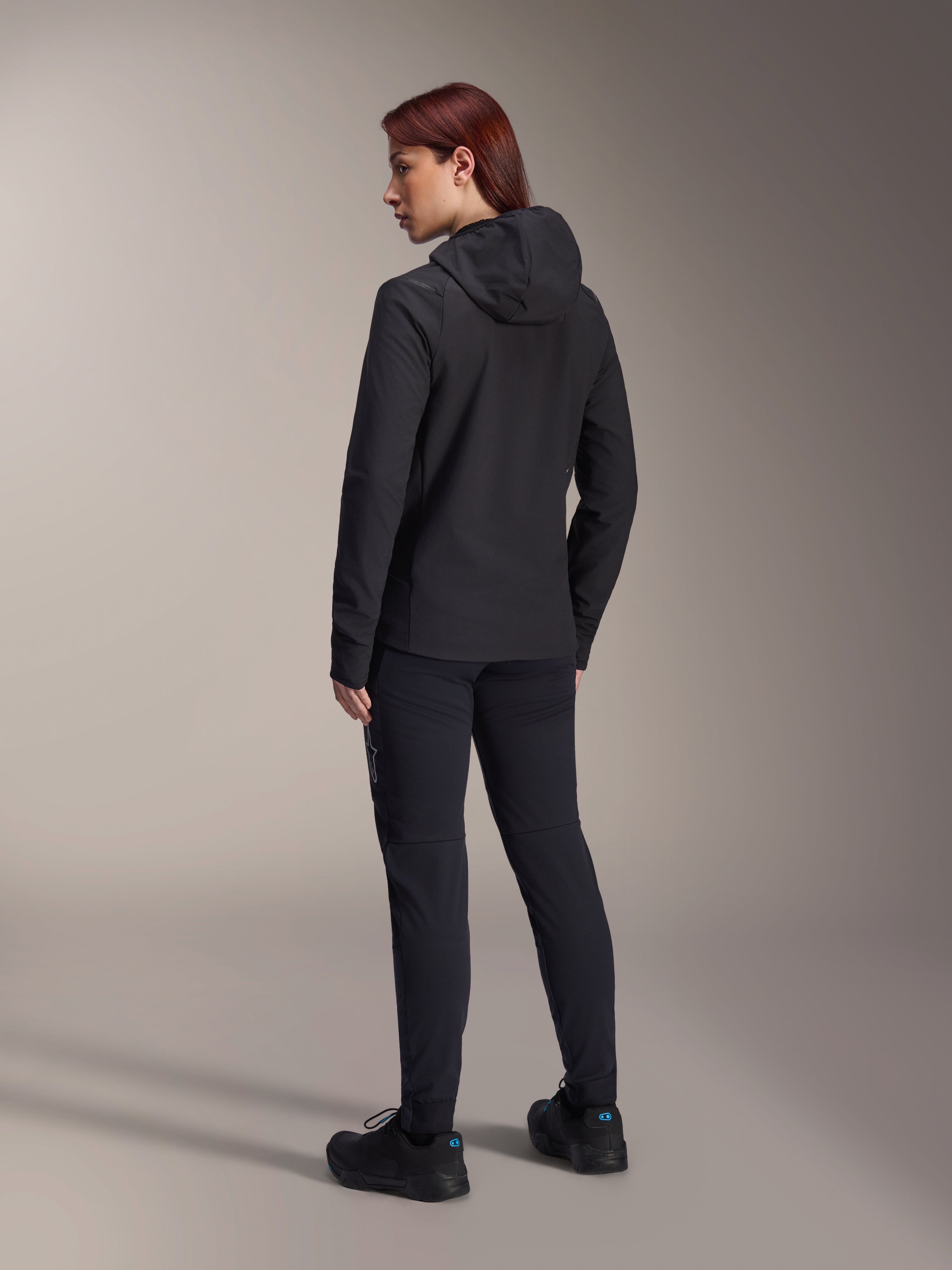 Alpinestars Stella A-Dura Thermal Jacket, Women's MTB cycling jacket, Black, back view highlighting the insulated hood and regular fit, worn with matching black pants and shoes, lightweight thermal insulation for cold-weather riding