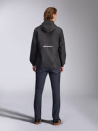 Alpinestars Speeder Chromium Windbreaker-Jacke, Schwarz, Rückansicht mit weißem Alpinestars-Branding in der Mitte, Modell mit Kapuze, getragen von einem Model mit dunkler Jeanshose, lässige, vom Motorsport inspirierte Jacke