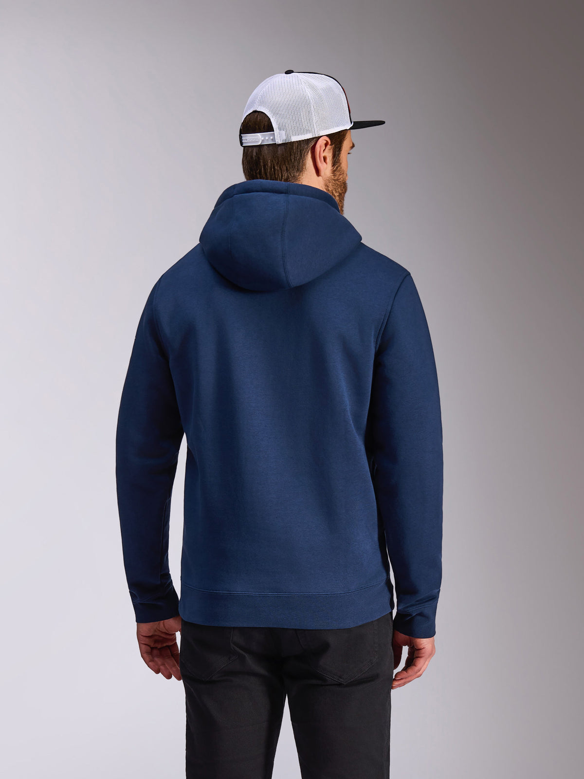Alpinestars Frontal Hoodie, marineblauer Fleece-Pullover, Rückansicht lässiger Streetwear, getragen mit schwarzer Hose und einer weiß-schwarzen Mesh-Kappe, modernes vom Motorsport inspiriertes Design