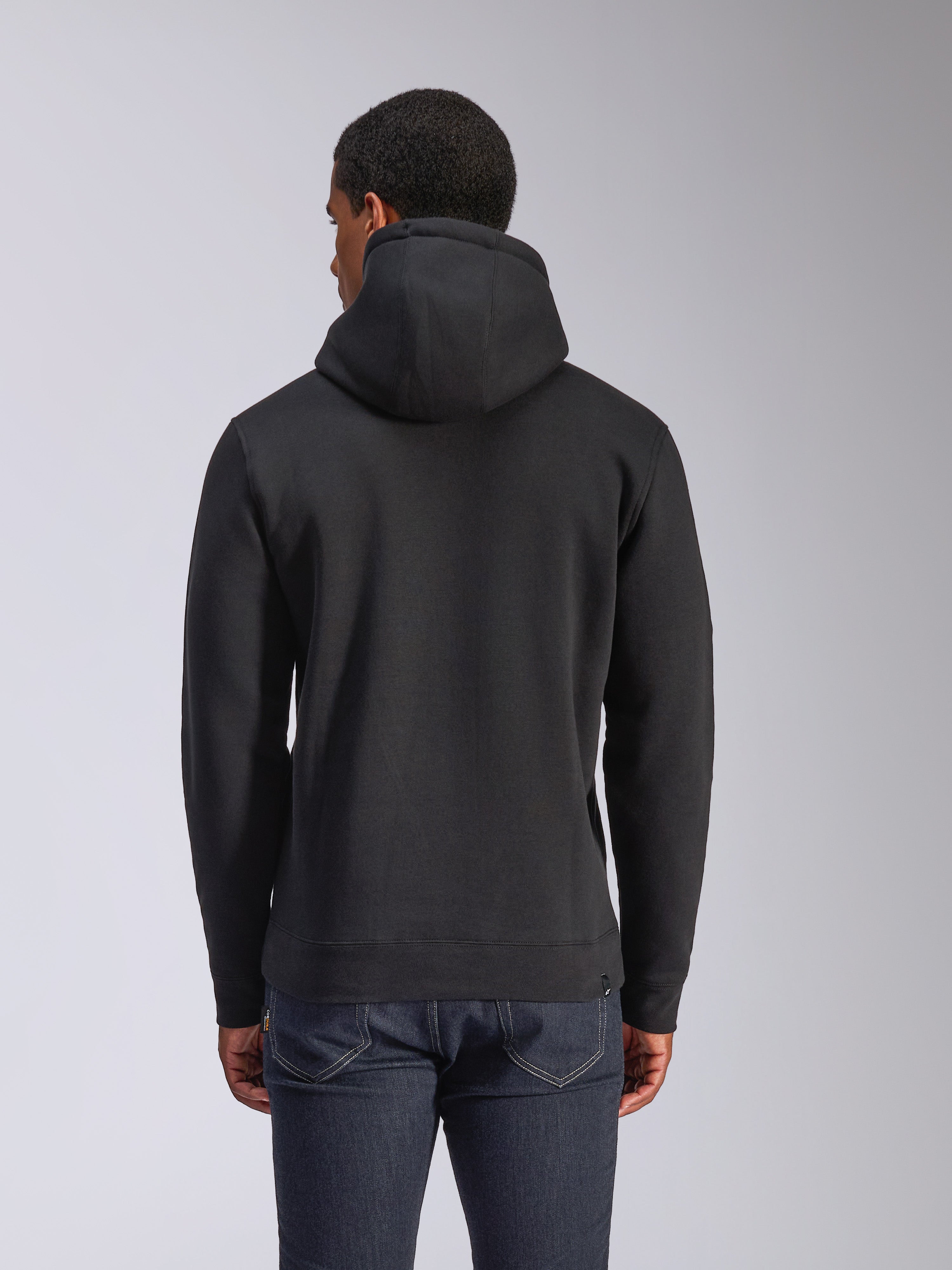 Alpinestars Blaze V3 Kapuzenpullover, Rückansicht eines schwarzen Fleece-Kapuzenpullovers, lässige Streetwear, mit Rippbündchen an Ärmeln und Saum, Kapuze mit Jersey-Futter, getragen mit dunkelblauen Jeans