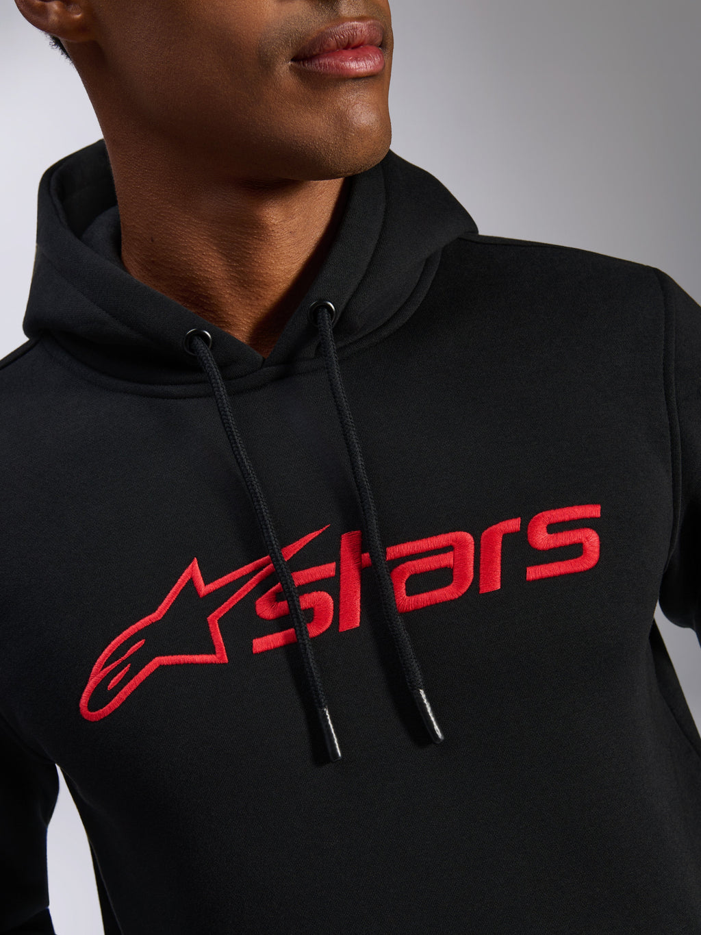 Alpinestars Blaze V3 Hoodie, Detailansicht des Brustbereichs, schwarzer Fleece-Stoff mit rotem linearen Alpinestars Logo-Druck, Kapuze mit Kordelzug und Tauchspitzen, lässige, vom Motorsport inspirierte Streetwear