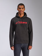 Alpinestars Blaze V3 Hoodie, Herren-Fleece-Kapuzenpullover, Schwarz mit rotem Alpinestars-Logo, getragen von einem Mann mit dunklen Jeans, Kapuze mit Kordelzug und Kängurutasche, lässige, vom Motorsport inspirierte Streetwear
