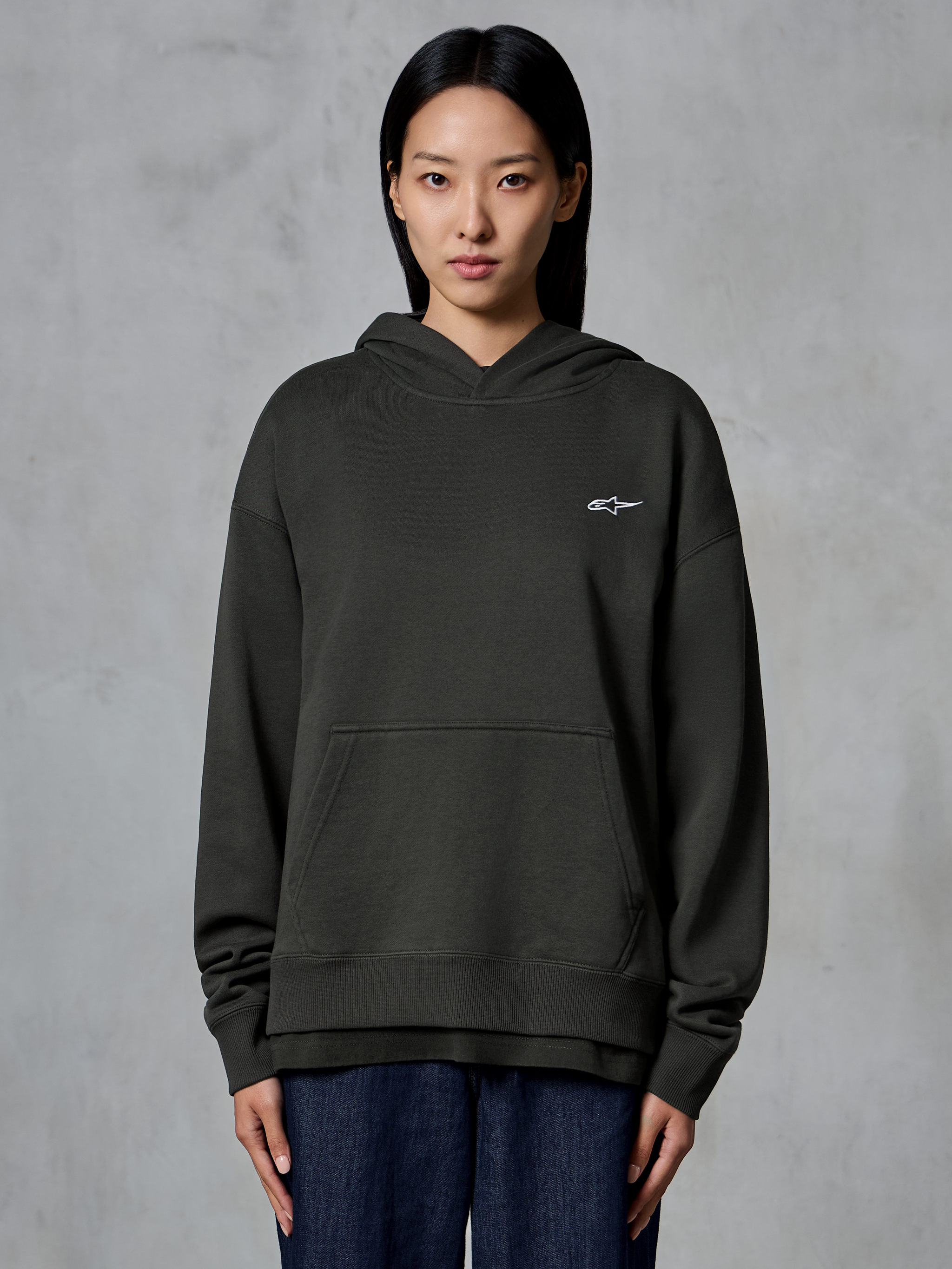 Alpinestars Essentials Ageless Hoodie, Off Black, von einem Model getragen, mit kleinem weißen Astars-Logo auf der Brust, Kängurutasche vorne, Stone-Wash-Finish, lässige Premium-Fleece-Streetwear