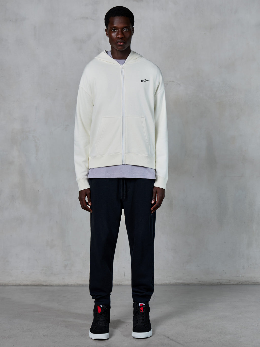 Alpinestars Essentials Ageless Zip Hoodie, Off White full-zip hoodie, relaxed fit with small black logo on chest, worn with black sweatpants and sneakers, casual motorsport-inspired streetwear.