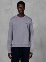 Alpinestars Essentials Ageless Crew, silbernes Rundhals-Sweatshirt von einem Model getragen, mit einem kleinen schwarzen Stern-Logo auf der Brust, entspannte Passform mit Rippbündchen und Saum, lässige Motorsport-Streetwear