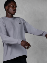 Alpinestars Essentials Ageless LS Tee, Langarm-T-Shirt, Silber, kleines schwarzes Logo auf der Brust, lässige vom Motorsport inspirierte Streetwear, getragen von einem Model vor einem grauen strukturierten Hintergrund