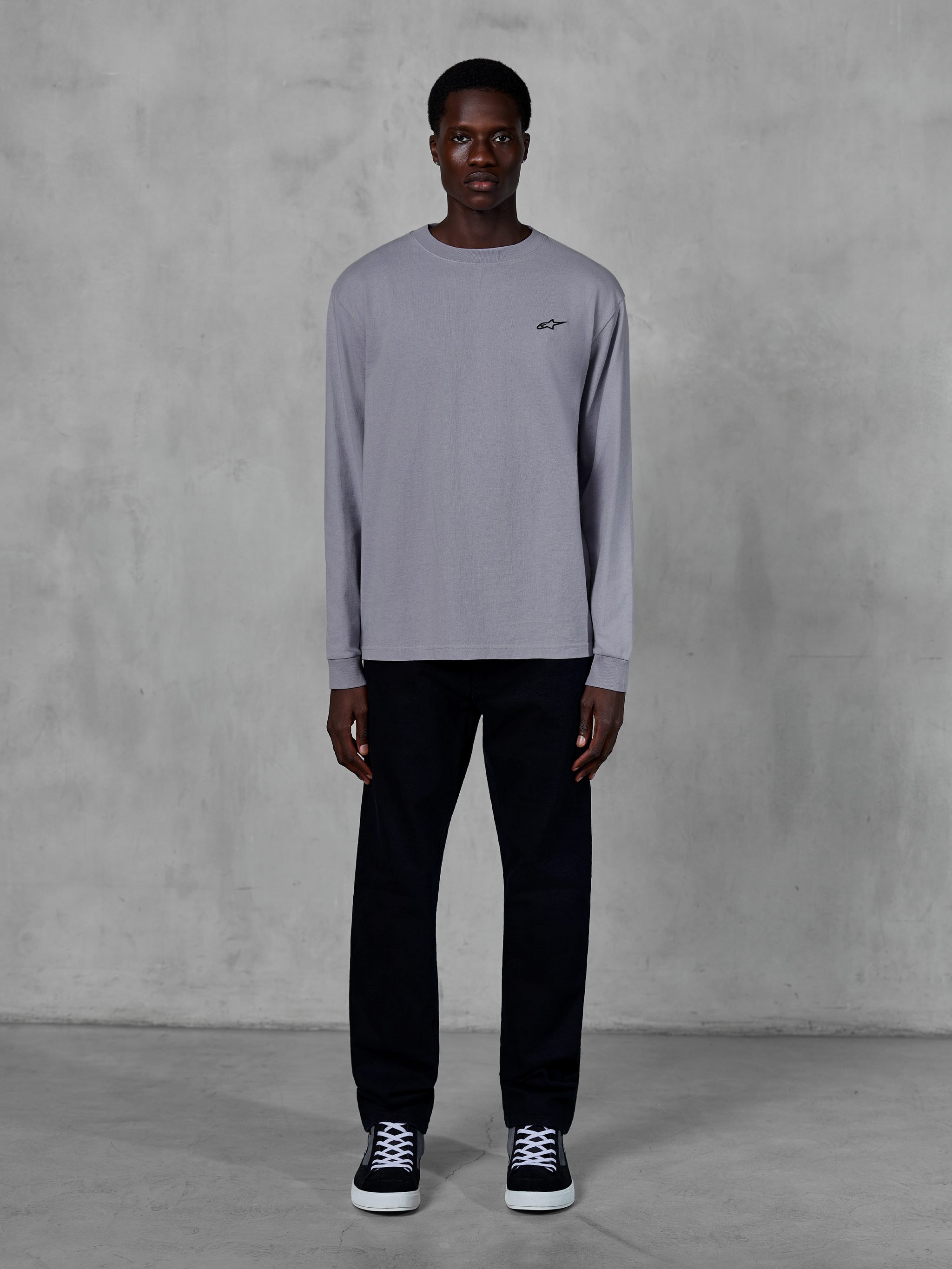 Alpinestars Essentials Ageless LS Tee, Langarm-T-Shirt, Silber, kleines schwarzes Alpinestars-Logo auf der Brust, Bio-Baumwolljersey mit Stone-Wash-Finish, getragen von einem Model mit schwarzer Hose und Sneakern, lässige Streetwear
