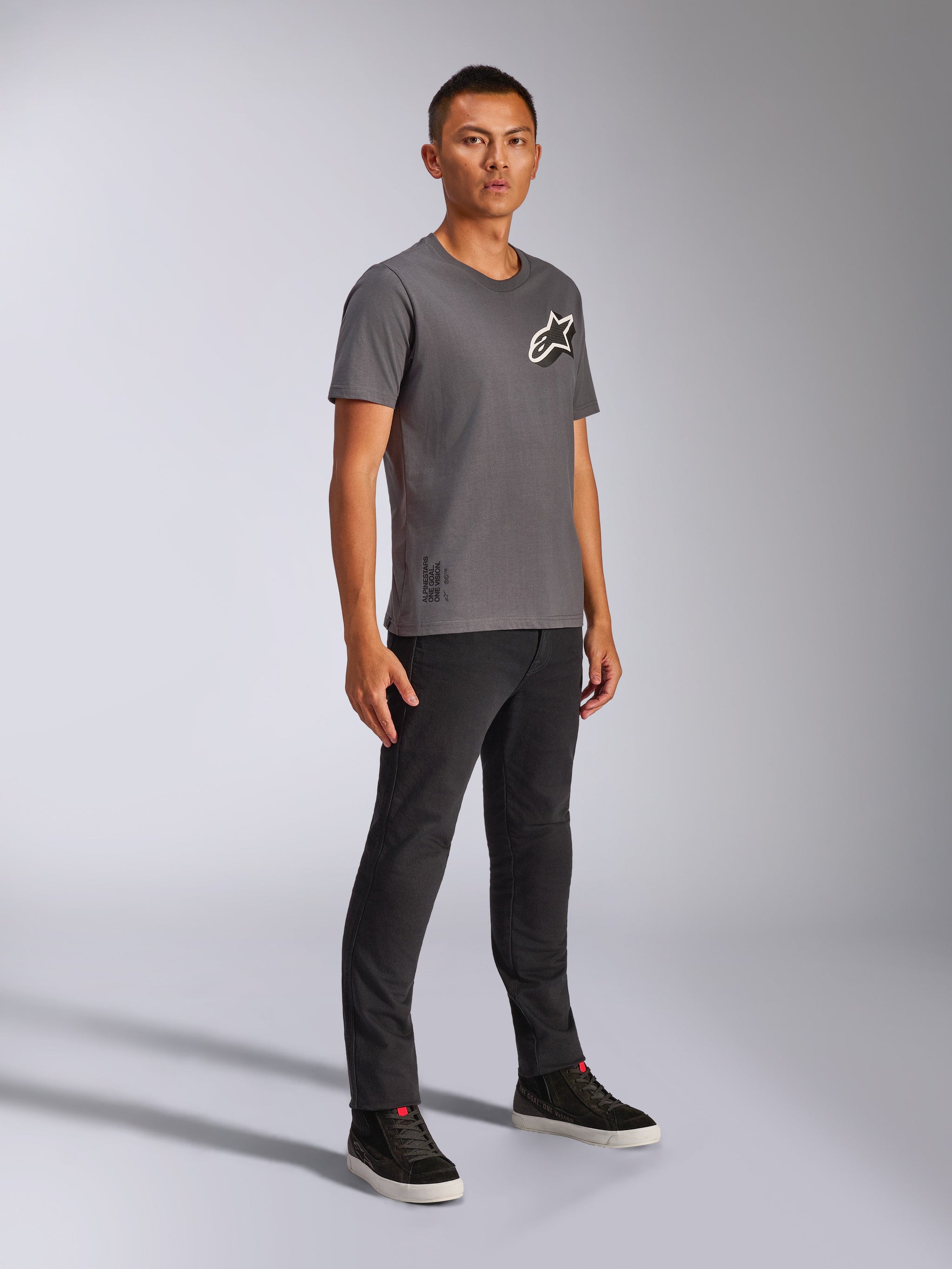 Alpinestars Shaded CSF Tee, Kurzarm-T-Shirt, Anthrazit, getragen von einem männlichen Model mit schwarzer Hose und dunklen Sneakern, mit schrägem weiß-schwarzem Astars-Logo, lässige vom Motorsport inspirierte Streetwear