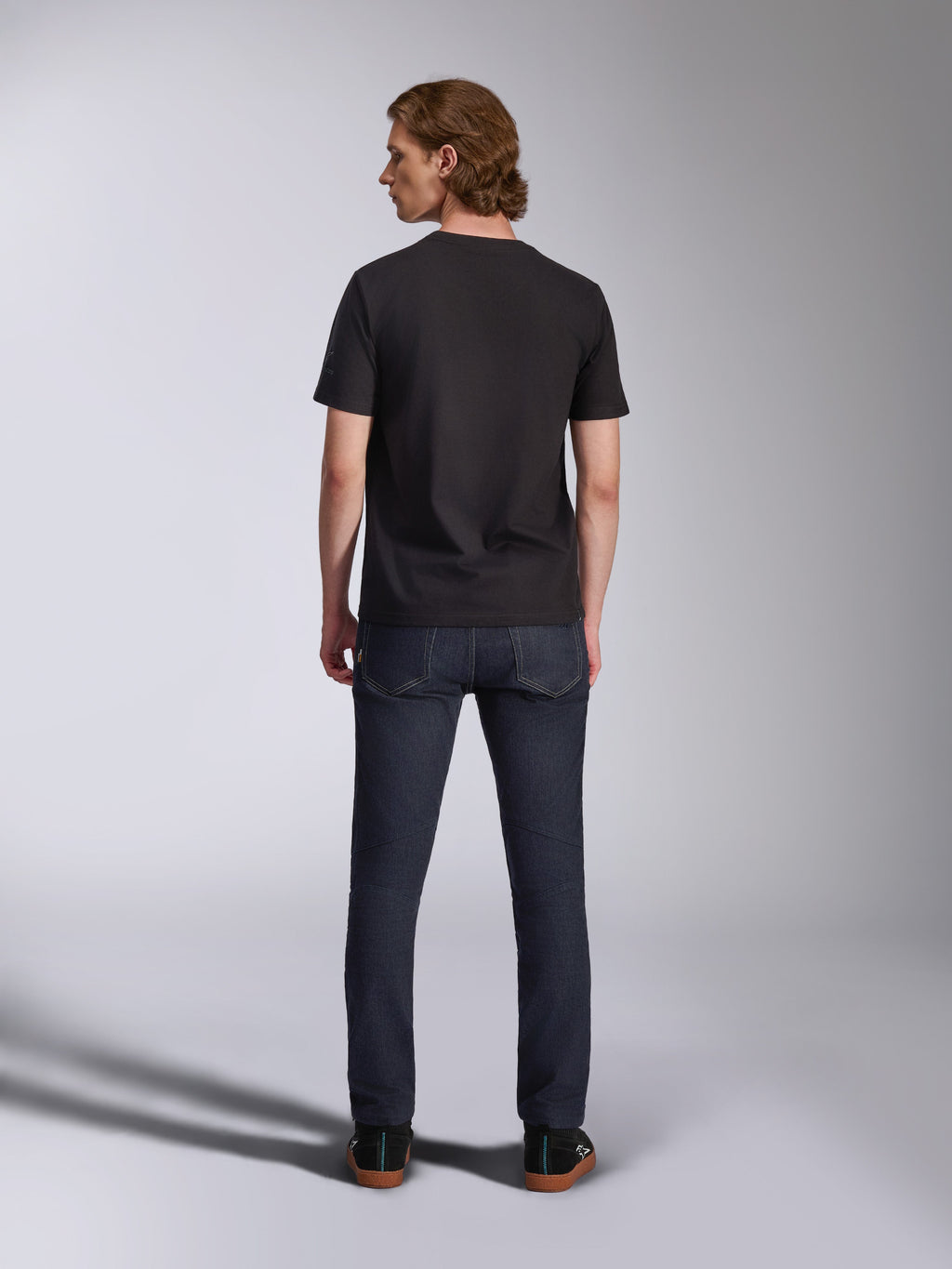 Alpinestars Global CSF T-Shirt, Kurzarm-T-Shirt in Schwarz, Rückansicht eines männlichen Modells, das das Shirt mit dunklen Denim-Jeans trägt, lässige vom Motorsport inspirierte Streetwear