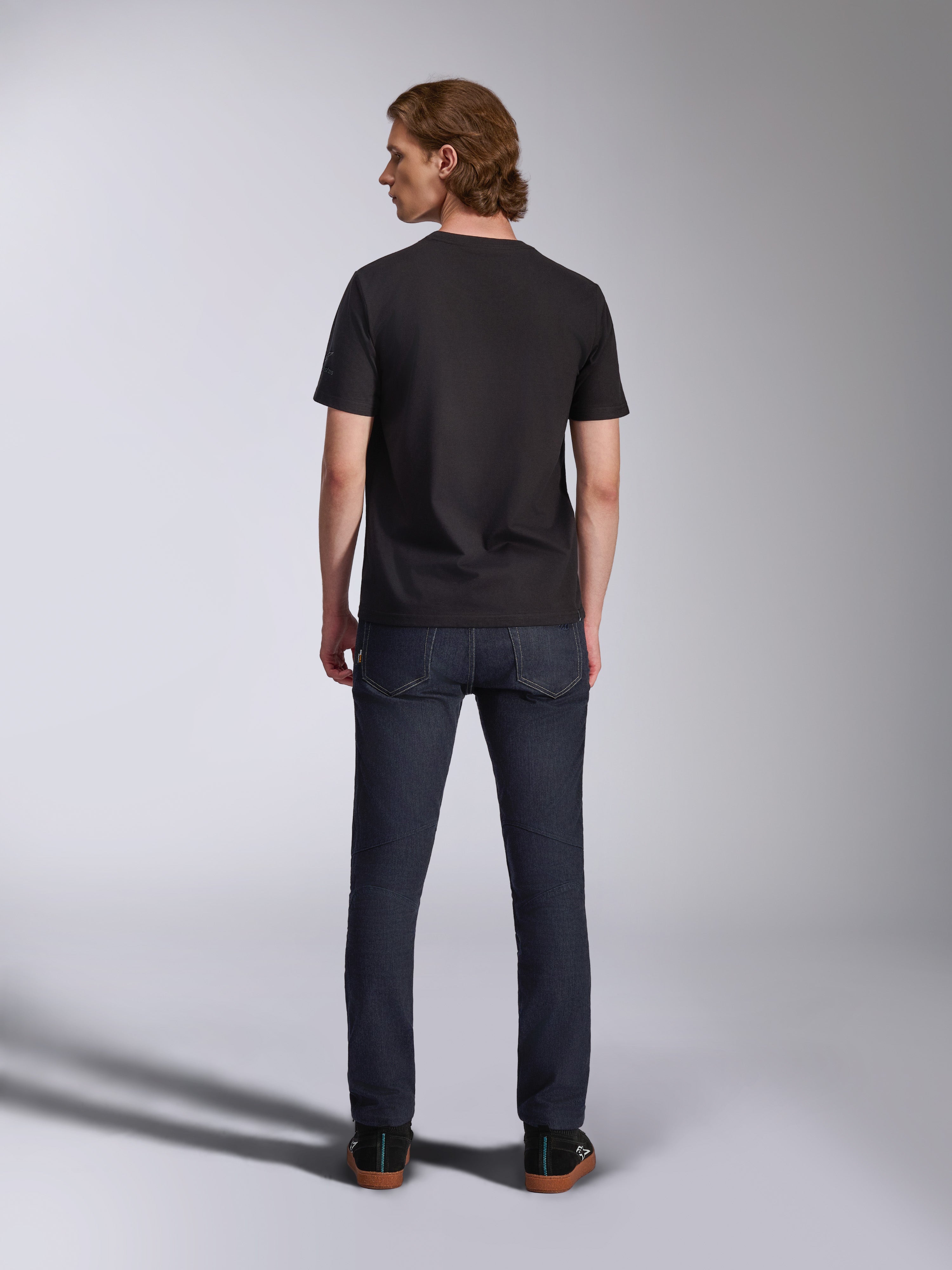 Alpinestars Global CSF T-Shirt, Kurzarm-T-Shirt in Schwarz, Rückansicht eines männlichen Modells, das das Shirt mit dunklen Denim-Jeans trägt, lässige vom Motorsport inspirierte Streetwear