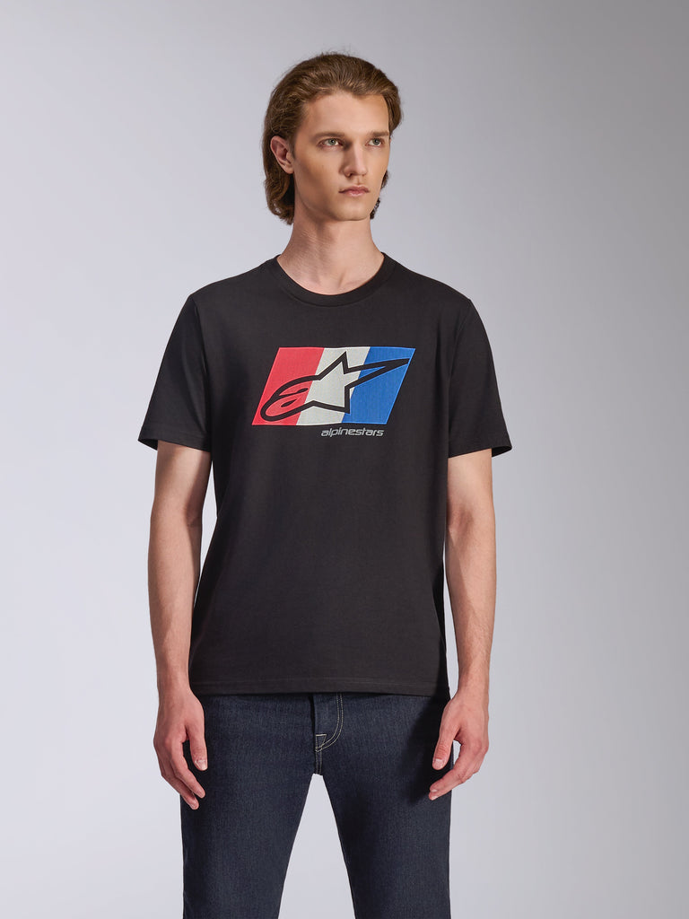 Alpinestars Global CSF T-Shirt, Kurzarm-T-Shirt, Schwarz, rot-weiß-blaue Ageless-Logo-Grafik, getragen von einem männlichen Model mit dunkler Jeans, lässige Motorsport-Streetwear