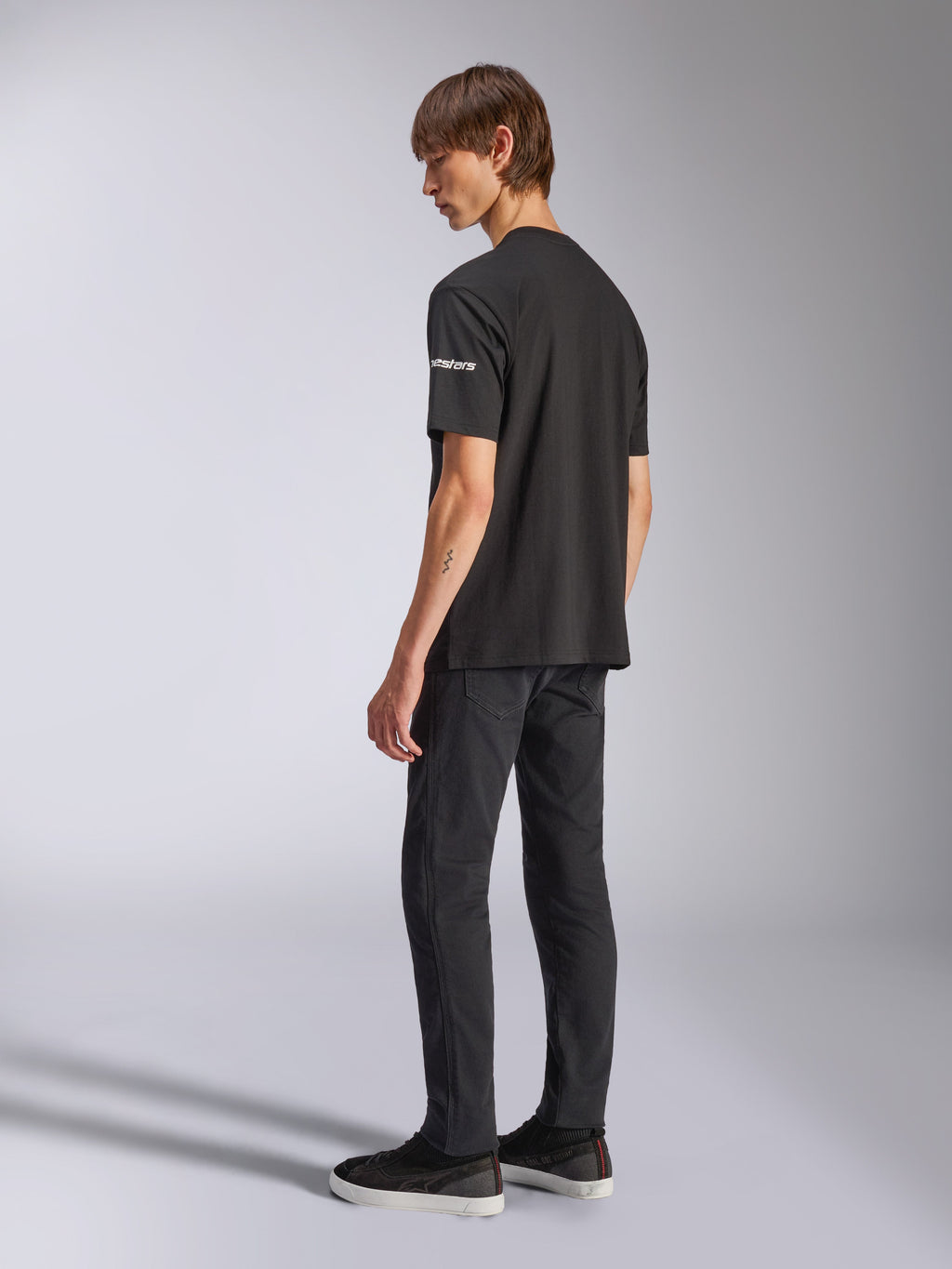 Alpinestars Frontal CSF Tee, Short Sleeve T-Shirt, Black, white astars branding on the sleeve, worn by model with black pants and shoes, casual motorsport-inspired design